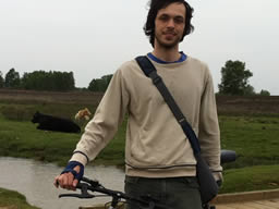Me standing with my bicycle, looking rather windswept. A ditch look with cattle are in the background.