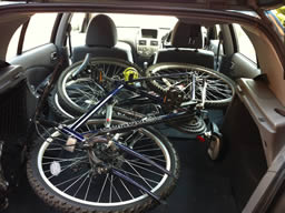 A pair of mountain bikes stacked in the back of my car, with front wheels removed.