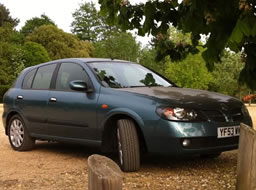 My green Nissan Almera parked on gravel under shade of a tree in evening sunlight.
