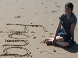 Fiona sitting next to her name, which she had written in the sand.