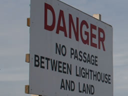 Big white sign says: &ldquo;DANGER. NO PASSAGE BETWEEN LIGHTHOUSE AND LAND.&rdquo;