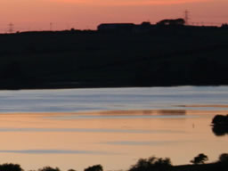 Optical illusion of a lake of gold as the sun sets, streaking the hazy sky with orange.