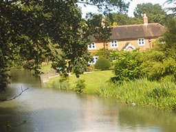 A rural detached house beside the tree-lined canal, viewed from an old brick bridge.