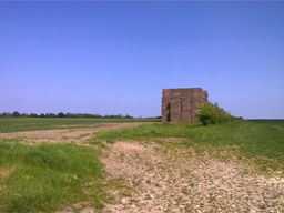A huge, square stack of oversized yet extremely neat hay bales is dwarfed by the fields and horizon.